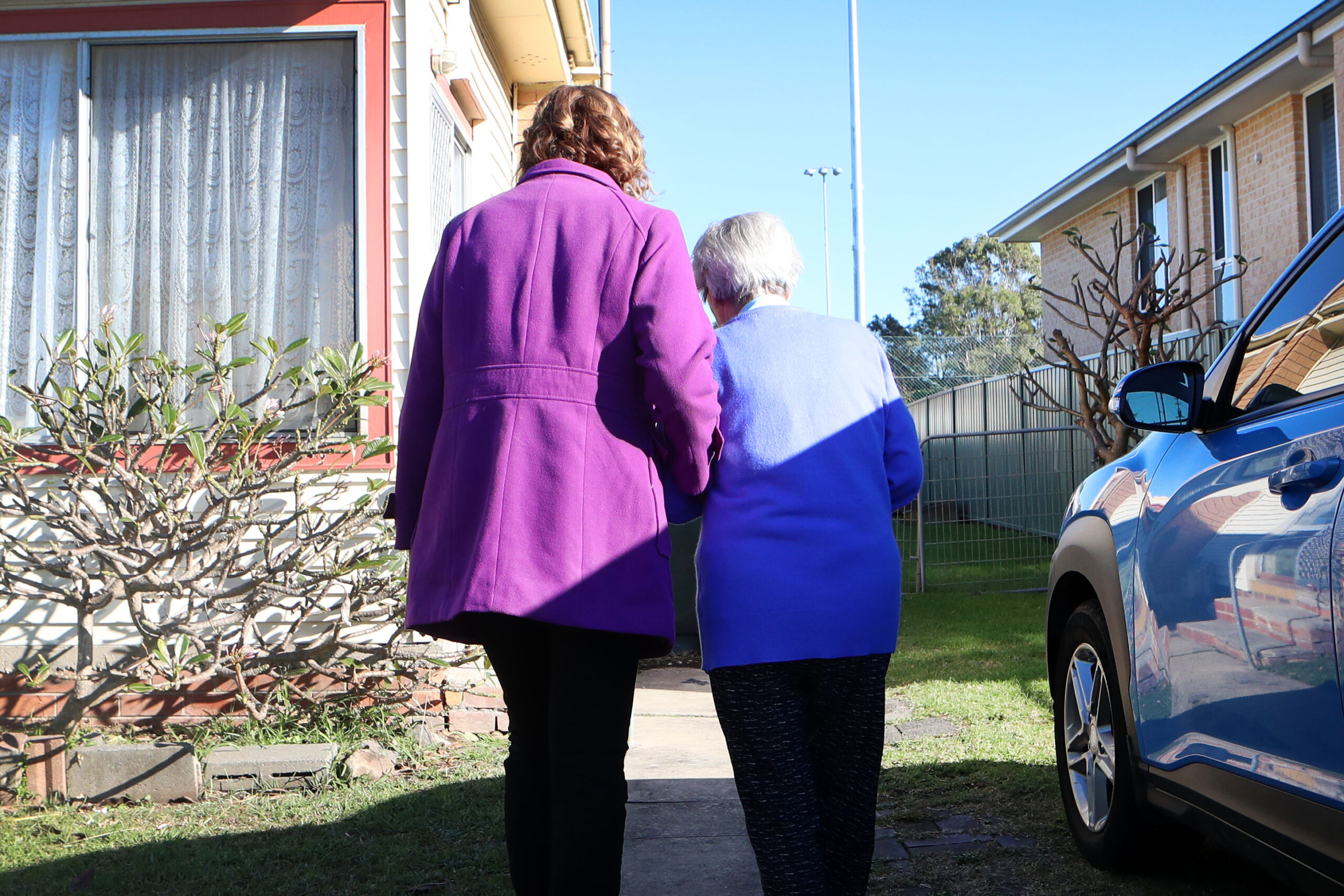 Caring staff member providing support to a resident, viewed from behind.