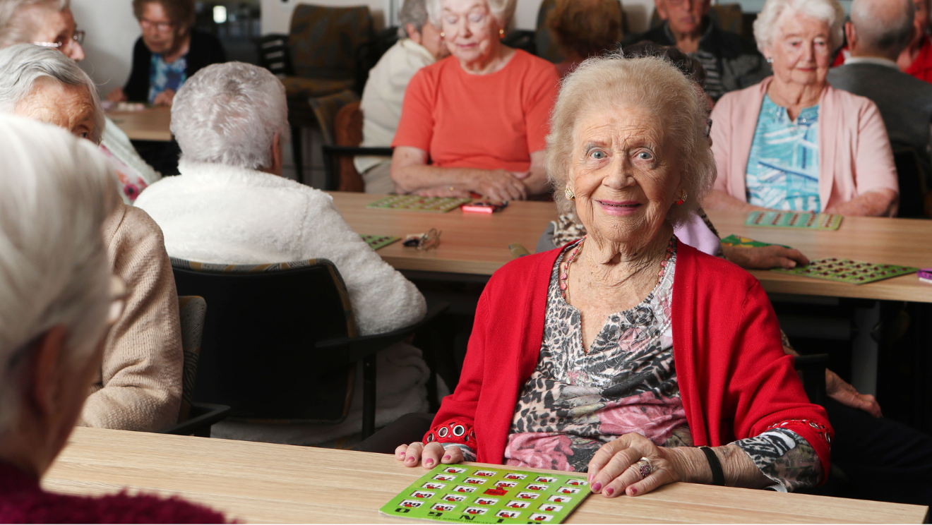 Warrigal aged care resident smiles at camera while playing bingo.