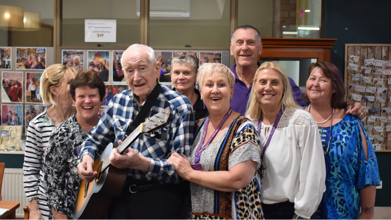 Warrigal social customers and staff smiling at the camera with a man holding a guitar