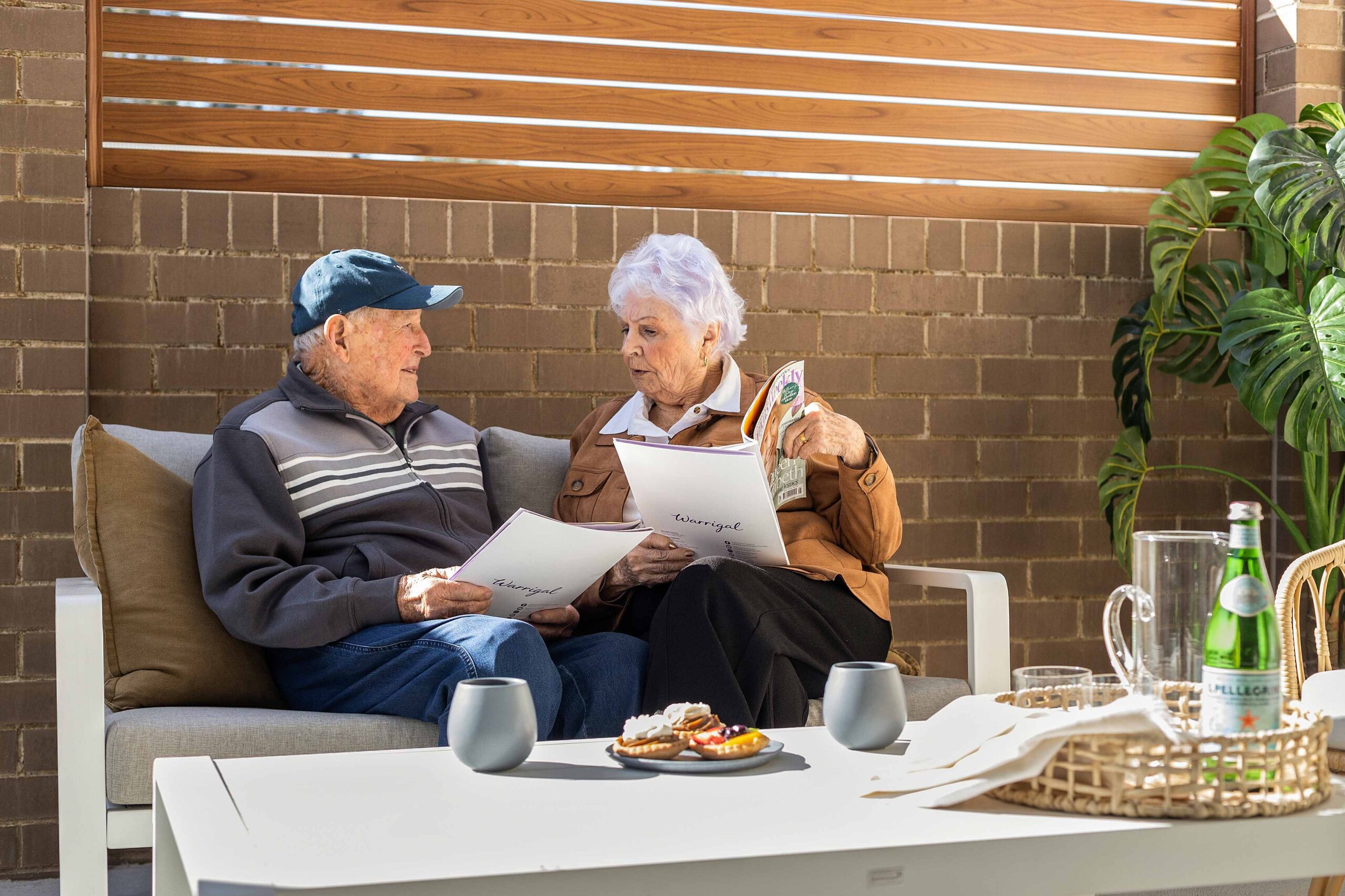 Woman reading magazine sits with man at Warrigal Lake South villa outside outdoors